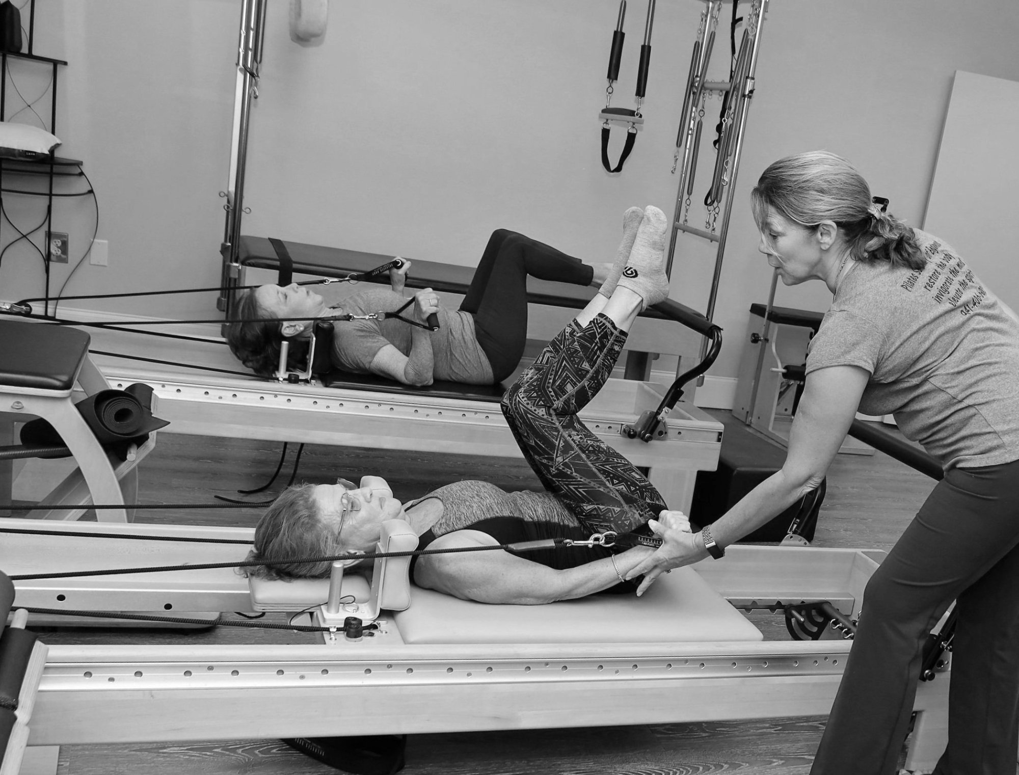 An instructor assisting two clients side by side on reformers during a duet session